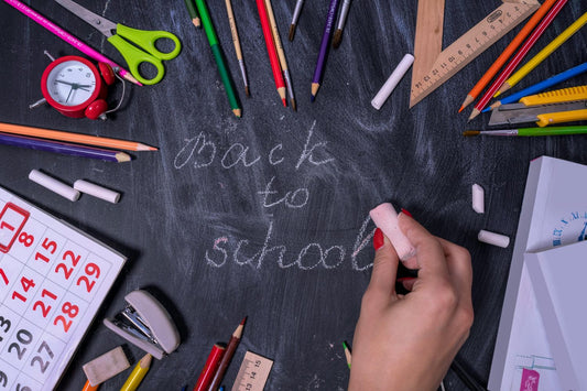 The words back to school being written on a chalkboard with school supplies around it