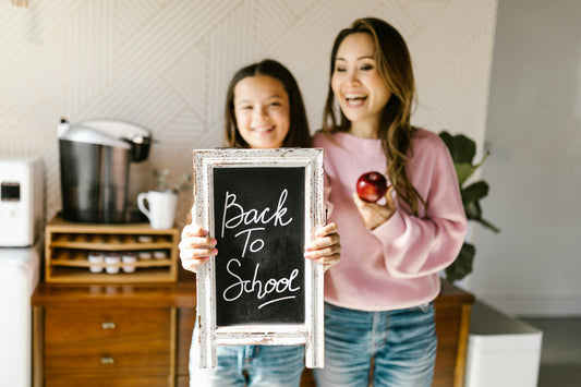 A young girl holds a "back to school" sign with her mom cheering her on